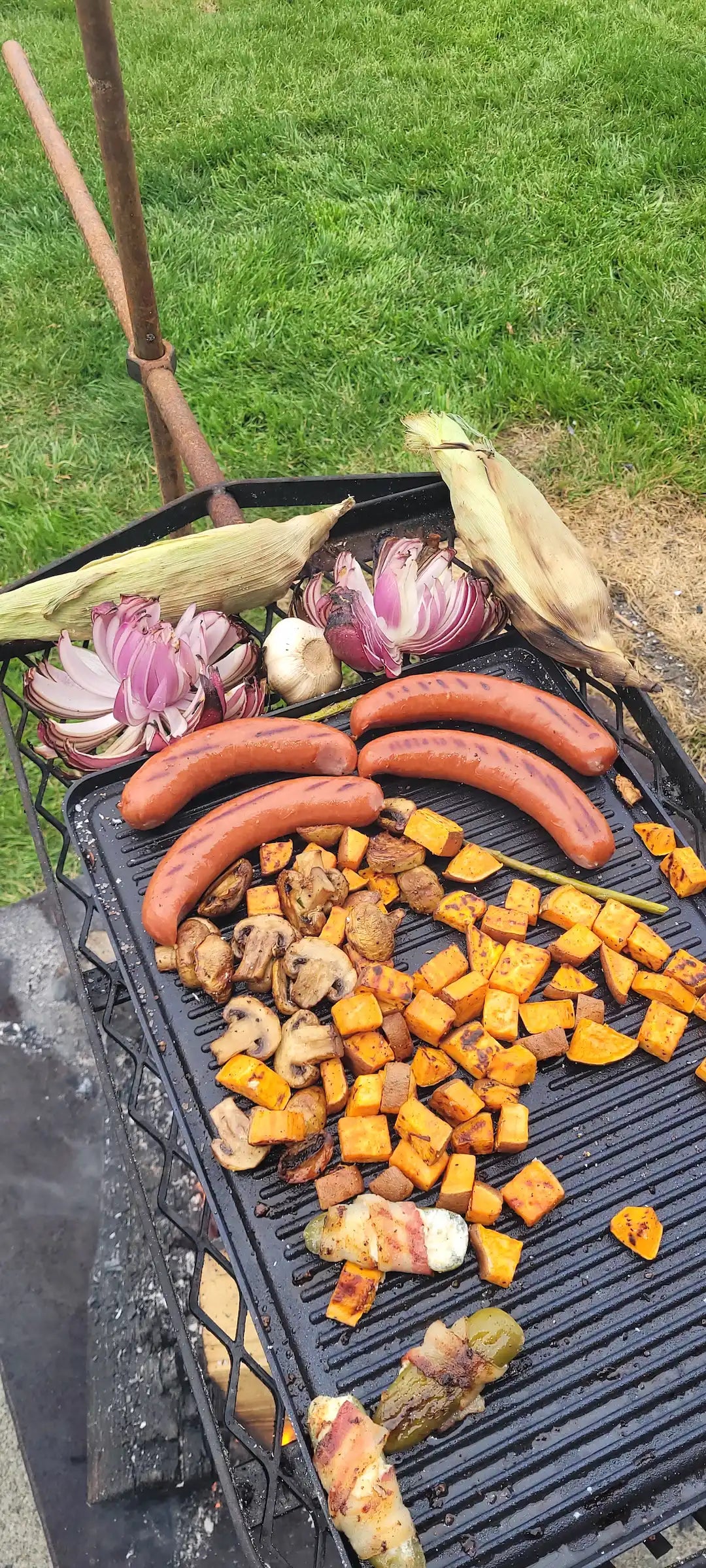 Corn onions and garlic on the Anvil grill with griddle that has dogs and potatos