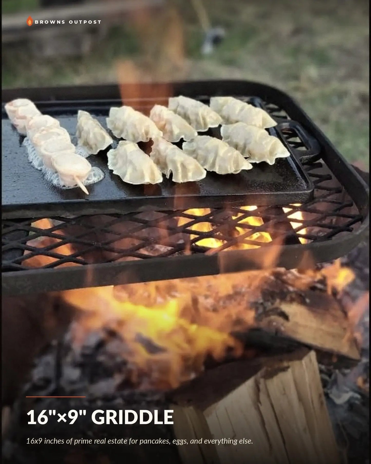 Browns Outpost 16x9 inch cast iron griddle set on a grill grate over a campfire, cooking pancakes, eggs and bacon. Text at the top reads 'Browns Outpost' and the bottom reads '16"×9" GRIDDLE' with a tagline reading '16x9 inches of prime real estate for pancakes, eggs, and everything else.'