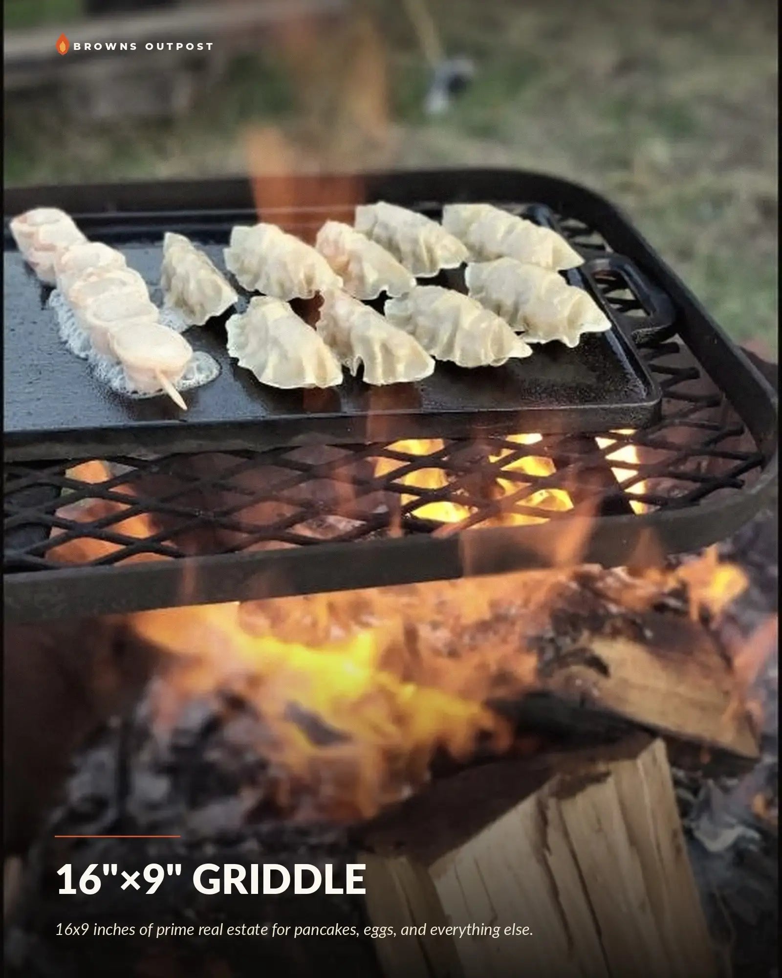 Browns Outpost 16x9 inch cast iron griddle set on a grill grate over a campfire, cooking pancakes, eggs and bacon. Text at the top reads 'Browns Outpost' and the bottom reads '16"×9" GRIDDLE' with a tagline reading '16x9 inches of prime real estate for pancakes, eggs, and everything else.'