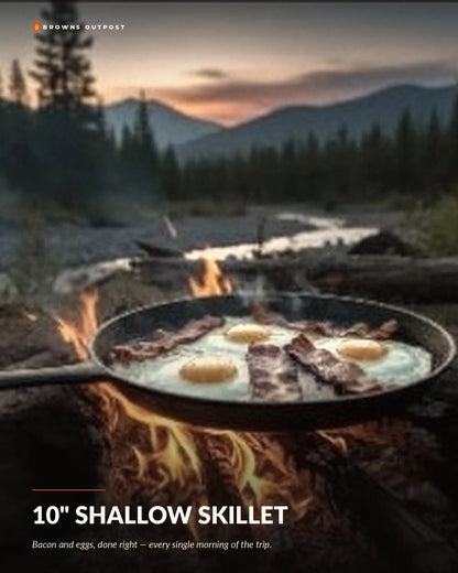 Browns Outpost 10-inch shallow cast iron skillet cooking bacon and eggs over a campfire. Text at the top reads 'Browns Outpost' and the bottom reads '10" SHALLOW SKILLET' with a tagline reading 'Bacon and eggs, done right — every single morning of the trip.'